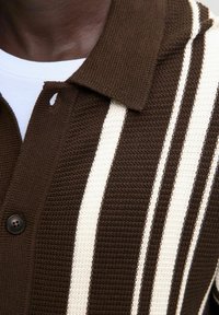 Braun- und cremefarbener gestreifter Strick-Polo-Shirt mit Knopfleiste am Hals und strukturiertem Stoffdetail.