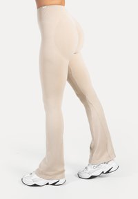Beżowe legginsy o gładkiej fakturze i rozszerzanym fasonie, z prążkowanym paskiem w talii i zaakcentowanymi konturami na tylnej części.