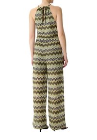 Green and brown zigzag-patterned jumpsuit with a halter neckline, open back detail, and wide-leg design. Soft, textured fabric.