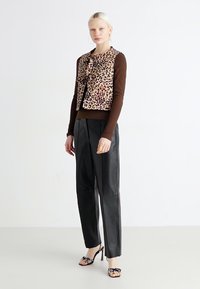 Prsluk s leopard uzorkom i detaljem mašne, u kombinaciji s smešnim dugim rukavima i širokim crnim kožnim hlačama. Crne sandale s petom ukrašene detaljima.