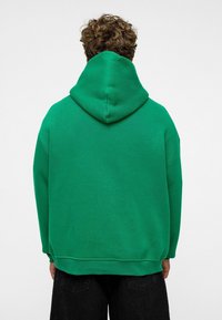 Groene hoodie met een grote, gebogen capuchon, een relaxte pasvorm, zachte textuur en geribde zoom. Gemaakt van een katoenmix voor comfort.