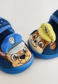 Blaue Plüschschuhe mit gestickten Cartoon-Hundegesichtern. Merkmale sind eine blaue Kappe und gelbe Akzente, eine weiche Textur und eine runde Form.