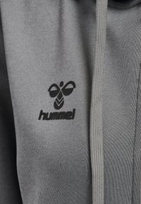 Gråt hættetrøje stof med sort hummel logo med stiliseret bi og tekst på brystet nær en snor.