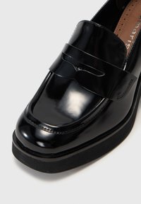 Μαύρες λουστρίνι loafers με στρογγυλή μύτη, που διαθέτουν ραμμένη λεπτομέρεια και επίπεδη πλατφόρμα. Το πάνω μέρος έχει λείο, γυαλιστερό φινίρισμα.