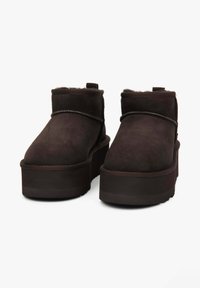Brązowe zamszowe botki za kostkę z grubą podeszwą na platformie, ozdobnym przeszyciem oraz krótkim futrzanym obszyciem wokół mankietu i języka.