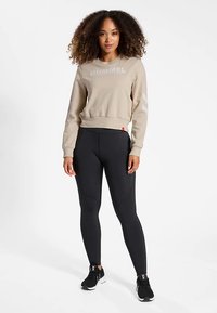 Beige sweatshirt med "HUMMEL"-logotyp, långa ärmar och ribbade muddarna, kombinerad med svarta leggings. Båda plaggen har en snygg, figurnära design.