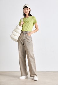Green t-shirt with "BOSS" print, high-waisted beige wide-leg jeans, white sneakers, and a cream puffer bag. Cap completes the outfit.