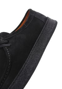 Zapatilla de ante negra con suela de goma texturizada, cordones en la parte delantera y un interior suave. Presenta una forma clásica redondeada.