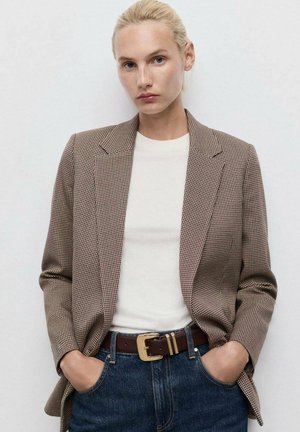 Hnědý kostkovaný blazer se strukturálními klopami, přes bílý top, spárovaný s džíny a hnědým páskem. Hladká textura s dobře přizpůsobeným střihem.