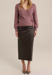 Rosa omlotttröja i mjukt stickat material, kombinerad med en stilren svart lädermidi-kjol med draperad design. Spetsiga klackskor fulländar looken.