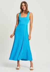 Aqua blue, ribbed maxi dress with a square neckline, pleats, and front button detailing. Features a flowy skirt and a fitted bodice.