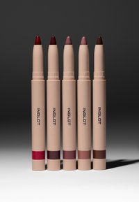 Cinq crayons à lèvres Inglot beige, debout, avec des teintes allant du rouge profond au marron sur un fond sombre en dégradé.