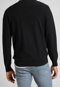 Schwarzer Strickpullover mit langen Ärmeln, gerippten Bündchen und Saum sowie einem runden Halsausschnitt, getragen über hellblauen Jeans. Glatte Textur.
