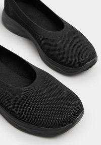 Schwarze Slipper mit strukturiertem Strick-Obermaterial, runder Zehenform und einer flexiblen Gummisohle für Komfort und einfache Tragbarkeit.