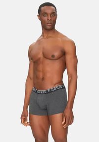 Caleçons gris avec une taille noire arborant le logo "GUESS". Tissu en coton extensible, design ajusté et texture lisse.