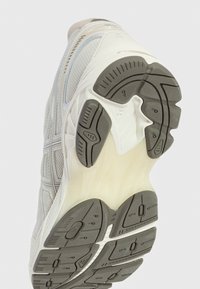 Bílá sportovní bota s texturovanou podrážkou, vybavená šedými gumovými trakčními polštářky a svrškem z síťoviny a syntetického materiálu. Akcenty tvoří světle modré linky.