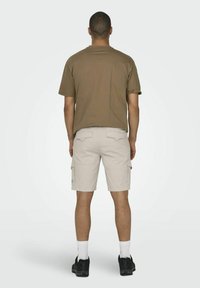 Brun crew-neck t-shirt og lysebeige cargo shorts med sidelommer, båret med hvide sokker og sorte sneakers, set fra ryggen.