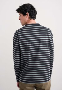 Musta pitkähihaisuus paita, jossa on turkoosit vaakaraitat. Ominaisuuksia ovat pyöreä pääntie ja rento malli. Muutoin yhdistetty vaaleanruskeisiin housuihin.