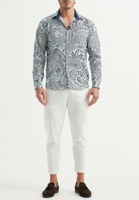 Chemise à manches longues avec un motif cachemire bleu clair et marine, design à col et fermeture à boutons, associée à un pantalon slim blanc.