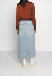 Jupe maxi en denim bleu clair avec taille haute, dotée de poches arrière et d'une coupe droite, assortie à une chemise en satin couleur rouille.