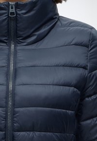 Крупен план на тъмносиньо подплатено яке с висок яка и предно затваряне с цип.