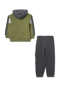 Felpa con cappuccio verde oliva con dettagli grigi e bianchi, abbinata a pantaloni jogger grigi con tasca laterale e cintura elastica.