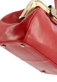 Red leather handbag with a glossy finish, featuring a gold-toned metal clasp and decorative hardware on the bottom. Smooth texture, structured design.