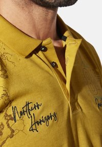 Yellow polo shirt with a textured fabric, featuring a traditional collar, black buttons, and embroidered "Northern Horizons" detail.
