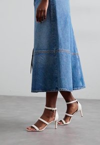 Gonna maxi in denim blu chiaro con cuciture a contrasto, abbinata a sandali bianchi con tacco dotati di sottili fasce e dettaglio con fibbia.