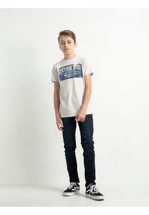 Hellgrau T-Shirt mit blauer Grafik "PETROL & CO" und Text, kombiniert mit dunklen Jeans und schwarz-weißen Sneakers.