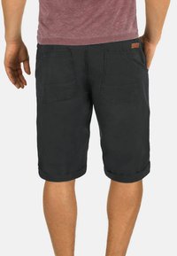 Shorts en denim gris foncé avec les poignets retroussés et deux poches arrière, portant une étiquette en cuir beige sur la taille. Design plat, style décontracté.