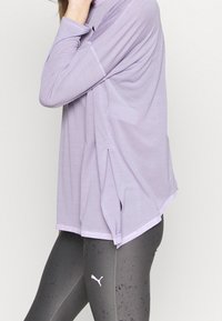 Light purple long-sleeve top with a relaxed fit and side slits, paired with dark gray leggings featuring a subtle speckled pattern and logo.