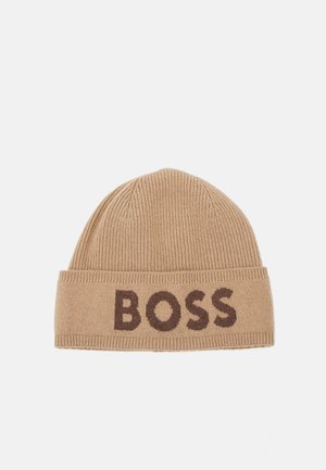 Pletená čiapka v béžovej farbe s lemom, na ktorom je tkané slovo "BOSS" v hnedej farbe. Mäkká textura, rebrovaný vzor a zaoblený tvar.