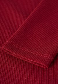 Tejido rojo con relieve y un sutil brillo, con un dobladillo cosido. La vista en primer plano resalta la textura y los detalles del material.