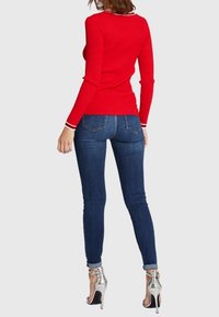 Punainen, ribbineulottu, pitkähihainen paita, jossa valkoinen kaulussomiste, yhdistetty tummansinisiin kapealahkeisiin farkkuihin ja hopeisiin korkokenkiin.