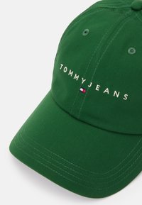 Zelena pamučna kapa s izvezenim natpisom "TOMMYJEANS". Ima šivenu viziru, ventilacijske rupe i logotip brenda sa strane.
