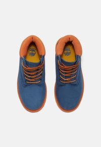 Zapatos de ante azul con detalles en naranja, cordones redondos y soporte acolchado en el tobillo en naranja. Suelas de goma planas con un patrón texturizado para mayor agarre.