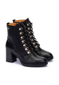 Botas de tobillo de cuero negro con tacón cuadrado, que presentan herrajes dorados decorativos y un detalle trenzado en el lateral. Cierre frontal con cordones.