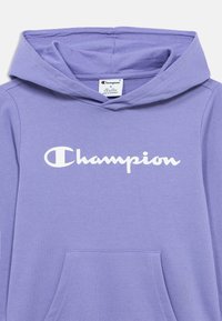 Μωβ φούτερ με κουκούλα από απαλό ύφασμα, με μπροστινή τσέπη και λευκό λογότυπο «Champion» στο στήθος. Κουκούλα με ρυθμιζόμενο κορδόνι.