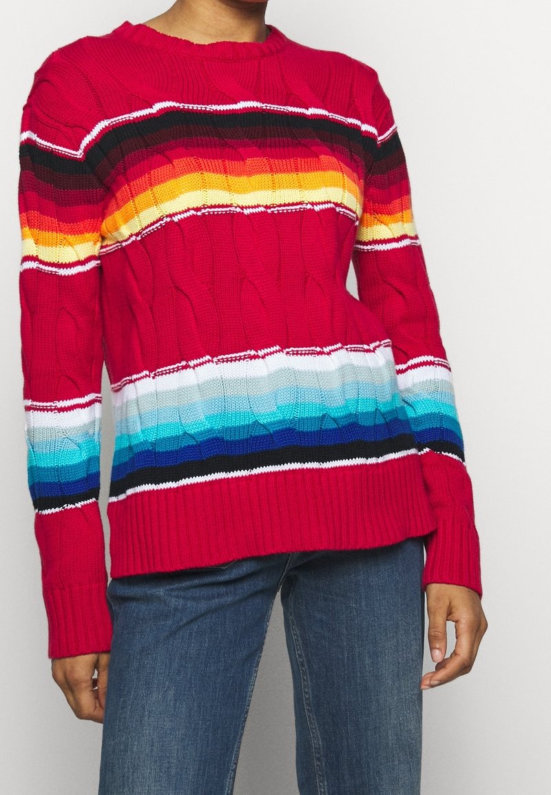 Pull en tricot rouge avec des rayures horizontales colorées en noir, orange, jaune, blanc et bleu, orné d'un motif torsadé texturé.