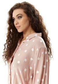 Light pink blouse featuring white polka dots, a button-down front, and a collared neckline. The fabric appears soft, with a relaxed fit.
