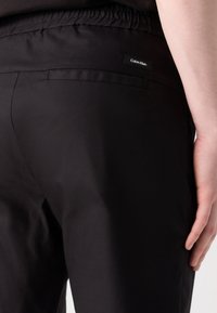Svarte, elastiske bukser med croppede ben og glatt tekstur. Har et lite Calvin Klein-logo på baklommen.