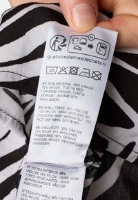 Black and white striped fabric care label on a garment, displaying care symbols and multilingual washing instructions. Textured, with clear printing.