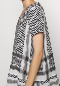 Czarny i biały top w wzory z dekoltem w kształcie litery V, krótkimi rękawami i luźnym krojem. Posiada geometryczne wzory i kontrastowe krawędzie.