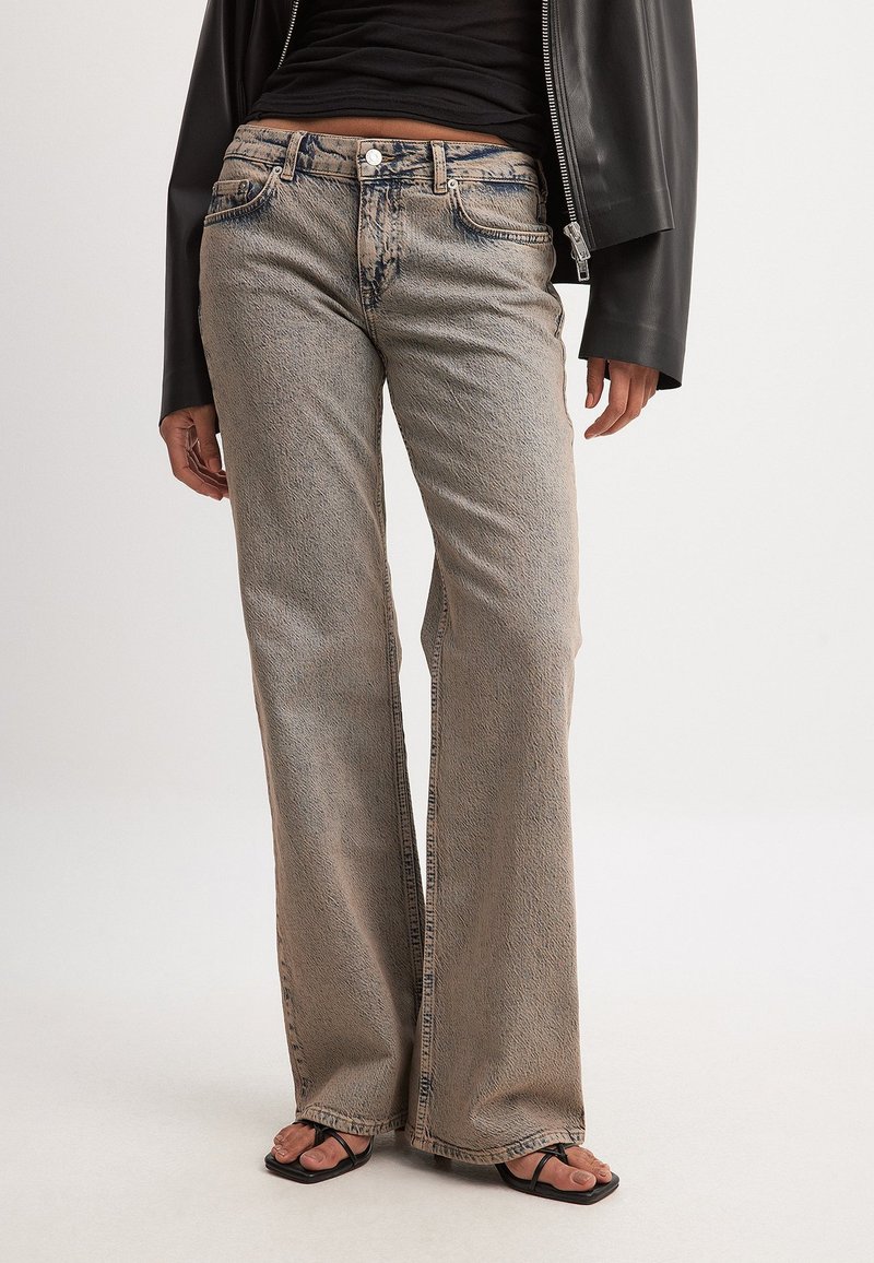 Gaiši pelēki platajām kājām džinsi ar teksturētu apdari, ar pieciem kabatām un metāla pogu aizdari, valkāti ar melnām sandālēm.