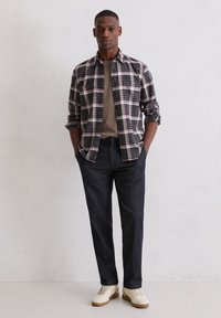 Kariertes Hemd in Schwarz, Weiß und Pink über einem beigen T-Shirt, kombiniert mit dunkler Hose und cremefarbenen Sneakern. Glatter Stoff und lockere Passform.