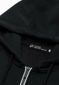 Sweat à capuche noir avec fermeture éclair, doublure en polaire, cordons de serrage et étiquette de marque "ombre performance" indiquant la taille moyenne.