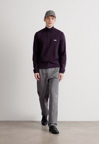 Ανδρική εμφάνιση με σκούρο μοβ φούτερ με φερμουάρ και ανοιχτό γκρι παντελόνι, συμπληρωμένο με γκρι καπέλο και μαύρα παπούτσια.