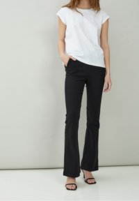 Vit, kortärmad, strukturerad topp i kombination med svarta utsvängda byxor; slätt tyg, mid-rise midja och en slank silhuett, förhöjd med öppna klackar.