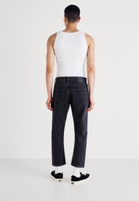 Vaqueros de mezclilla negra con corte recto, cinco bolsillos y un parche en la parte trasera de la cintura. Combinados con zapatillas negras y calcetines blancos.